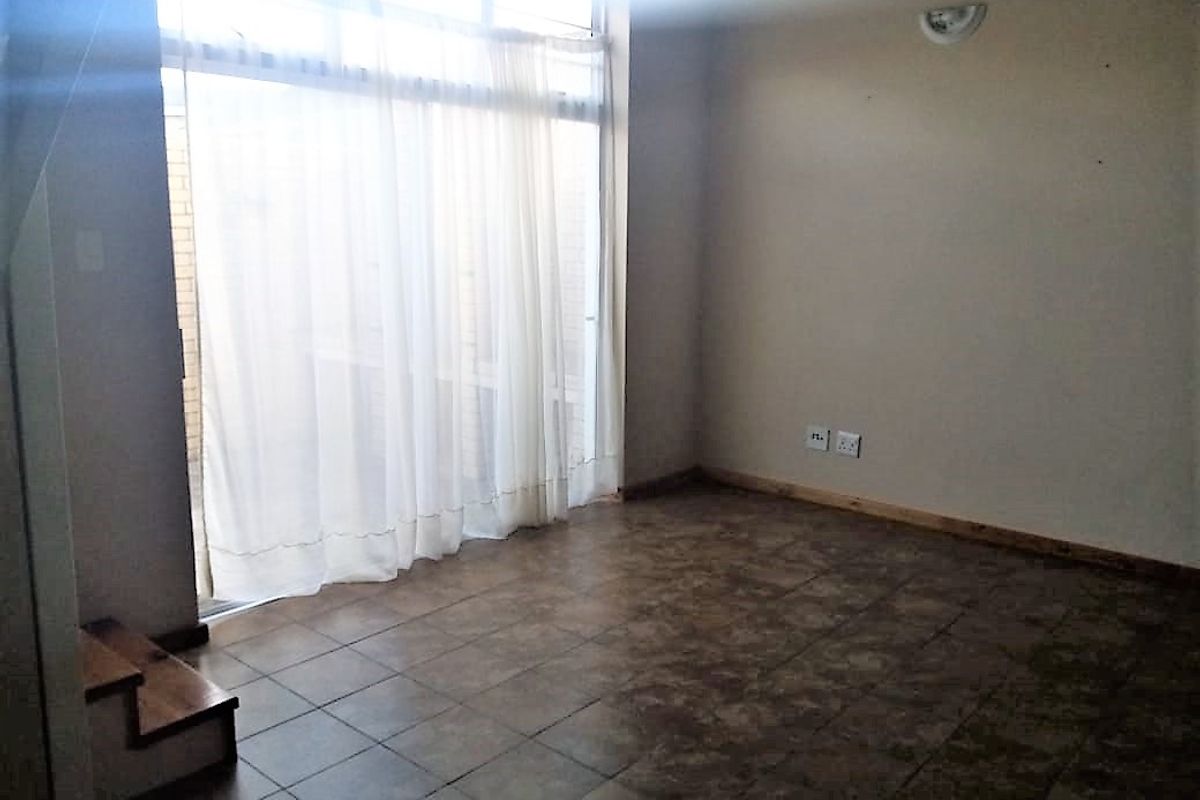 An empty living room featuring tiled flooring, a large sliding glass door providing natural light, and an integrated staircase.