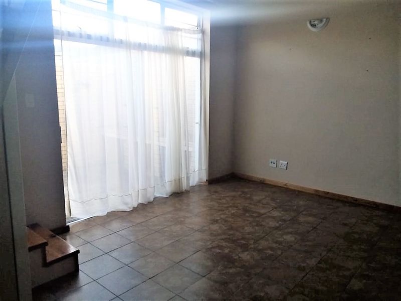 An empty living room featuring tiled flooring, a large sliding glass door providing natural light, and an integrated staircase.