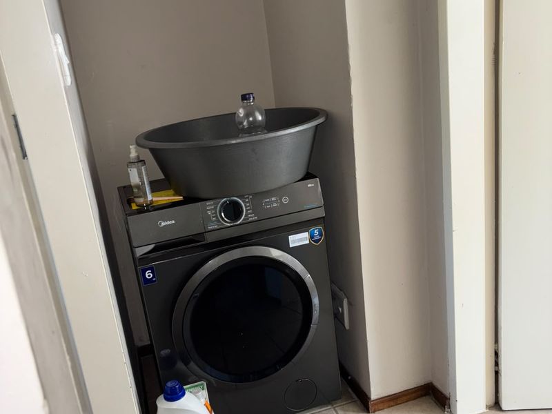 A compact laundry alcove featuring tiled flooring and space for a washing machine.