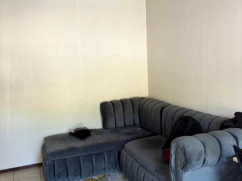 A living room area featuring tiled flooring and a simple ceiling light fixture, currently showing signs of wear on the wall surfaces.