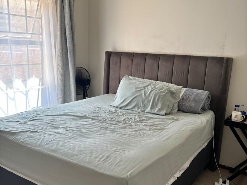 A functional bedroom featuring tiled flooring and a window with security bars, providing natural light and ventilation.