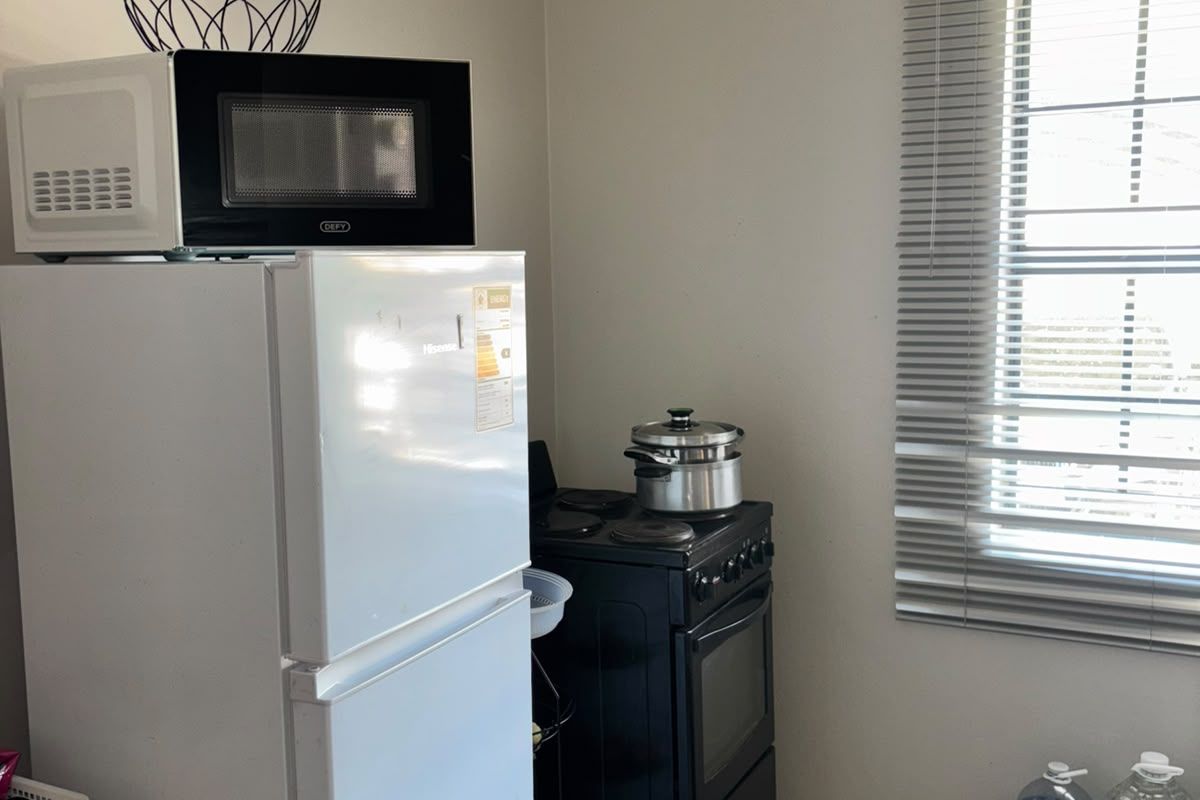 A functional kitchen area featuring tiled flooring, a freestanding stove, and a window fitted with venetian blinds.