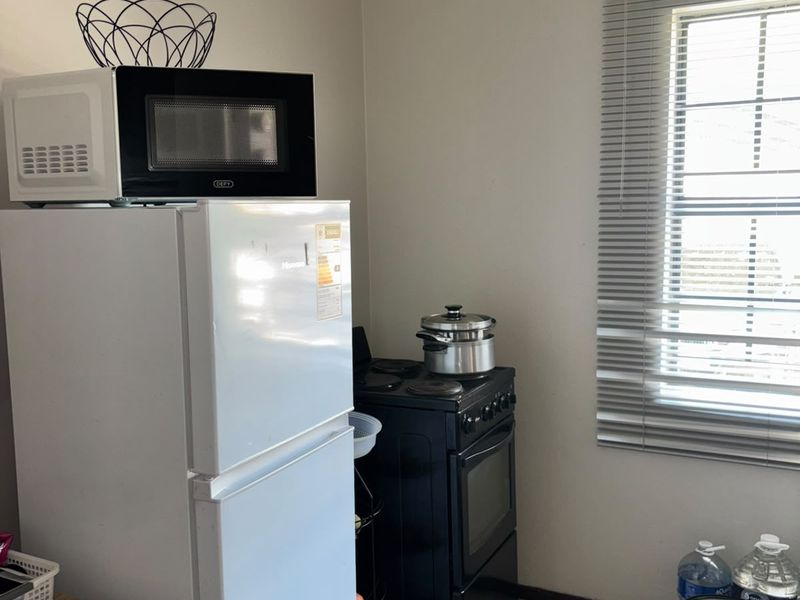 A functional kitchen area featuring tiled flooring, a freestanding stove, and a window fitted with venetian blinds.