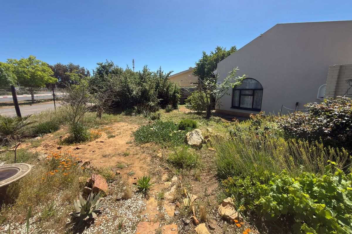 A view of the rear garden area featuring established landscaping, a masonry wall, and an arched window on the side of the house.