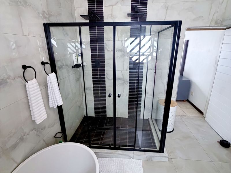 Modern bathroom featuring a sleek walk-in shower with black framing, dual shower heads, and a contemporary freestanding bathtub with high-quality tiled finishes.