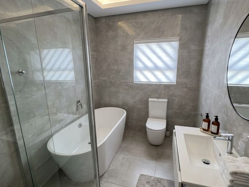 Modern bathroom featuring a freestanding bathtub, glass-enclosed shower, wall-mounted toilet, and a sleek vanity with integrated sink, finished with contemporary grey tiling.