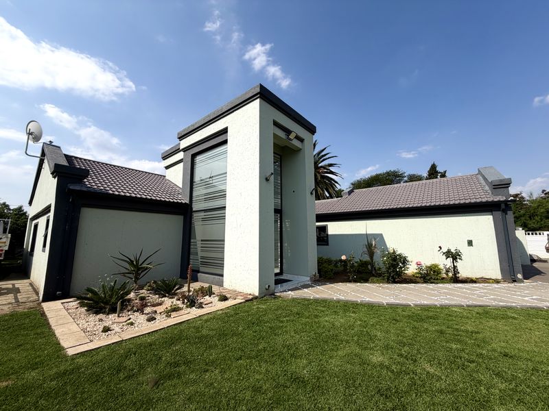 A modern front elevation featuring a prominent central tower structure, tiled roof, paved walkway, and well-maintained garden area.