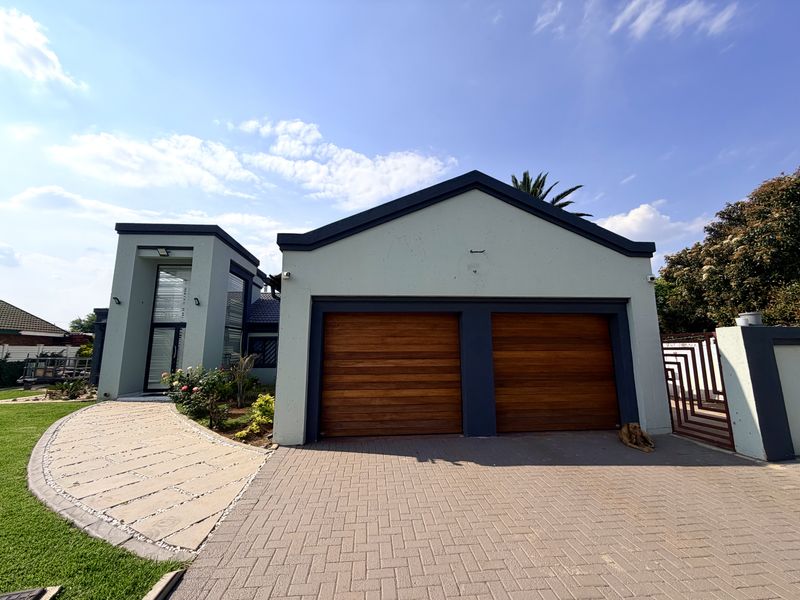 Front elevation of a modern home featuring a double garage with timber doors, a paved driveway, and a stone walkway leading to the entrance.