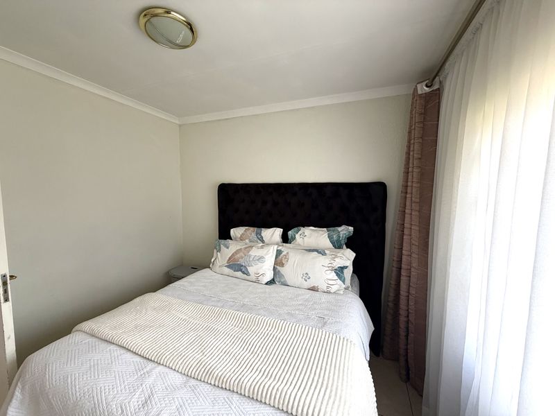A cozy bedroom featuring neutral wall tones, tiled flooring, and a ceiling light fixture, providing a comfortable and functional sleeping space.