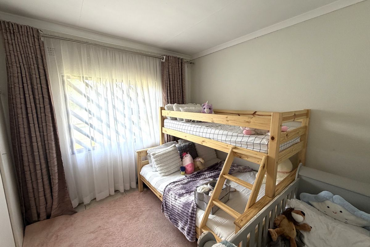 A functional bedroom featuring a window with security bars and installed curtain rails, providing a comfortable space for rest.