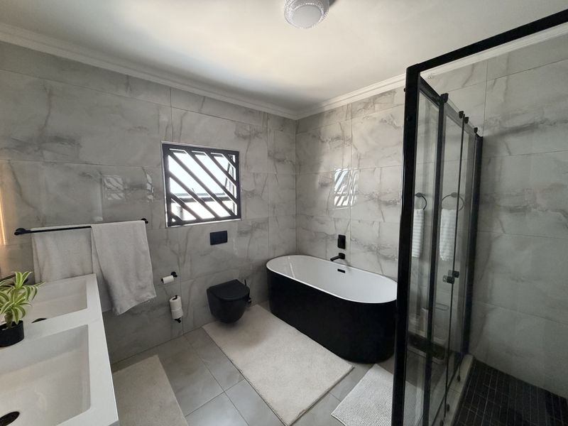 Modern bathroom featuring a sleek freestanding bathtub, walk-in shower with black frame, double vanity, and contemporary marble-look wall tiling.