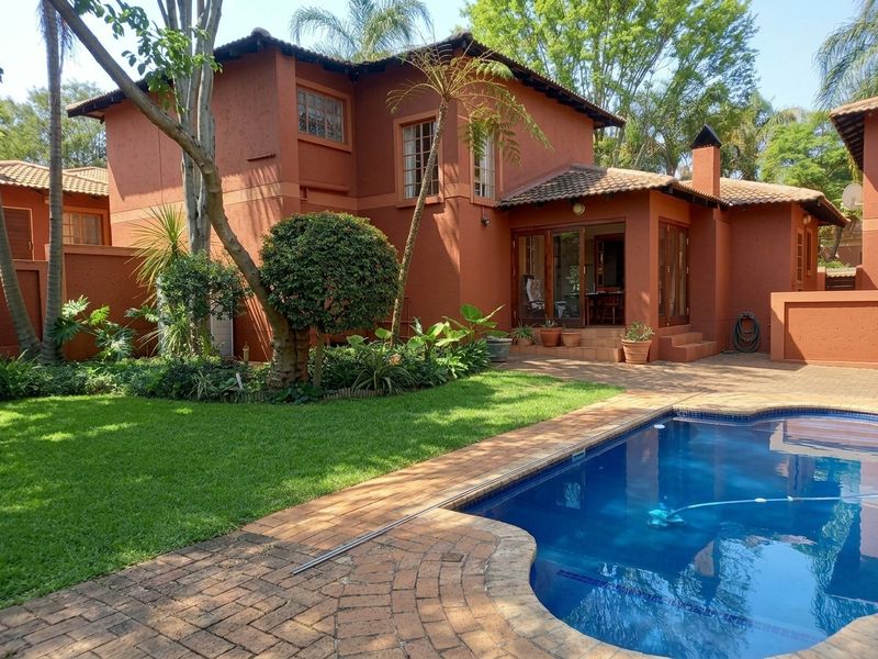 Rear view of the townhouse featuring a private swimming pool, landscaped garden, brick-paved patio area, and classic terracotta-finished exterior walls.
