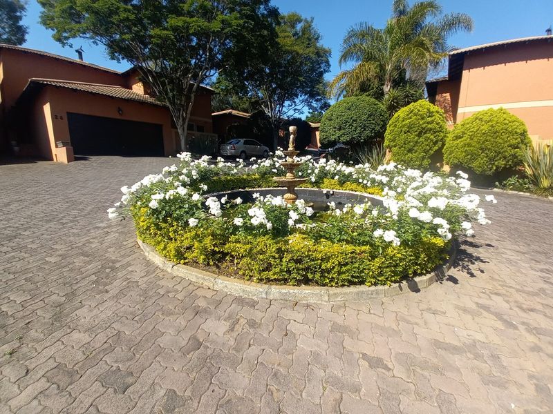 A well-maintained front driveway featuring a central circular garden bed with a water fountain, surrounded by established landscaping and paved access to the garage.