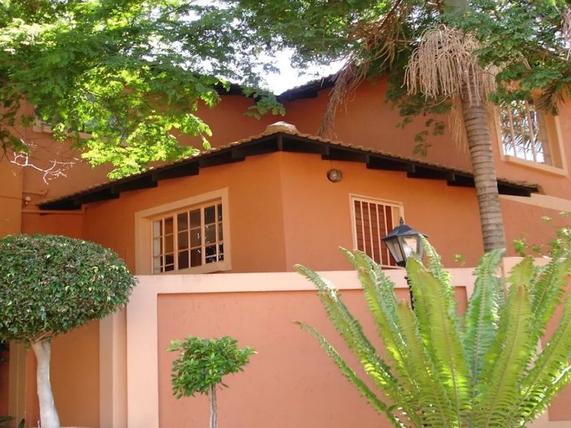 Front exterior view of a townhouse featuring terracotta roof tiles, security bars on windows, and a perimeter wall.