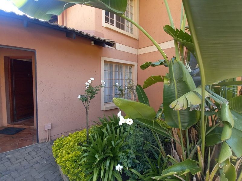 Front entrance of the townhouse featuring a paved walkway, stucco facade, and established garden beds with security bars on the windows.