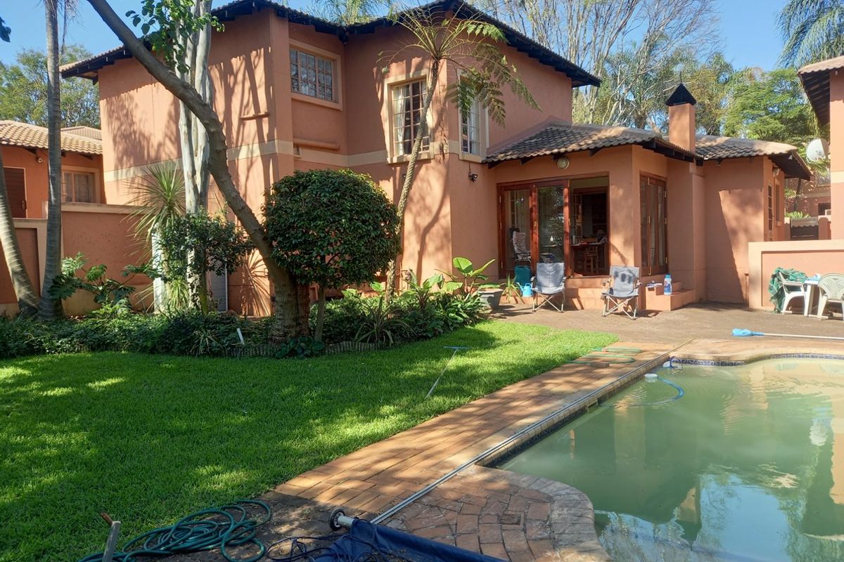 Rear view of the townhouse featuring a private swimming pool, paved patio area, and established garden with mature trees.