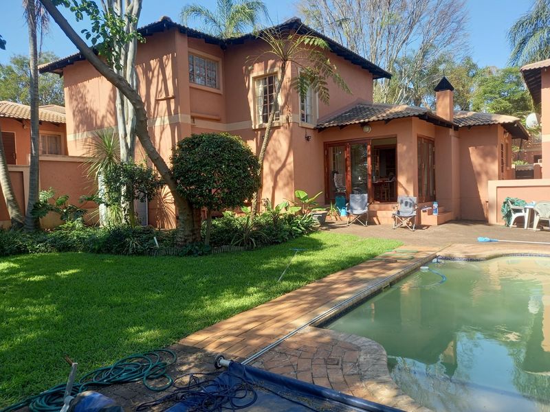 Rear view of the townhouse featuring a private swimming pool, paved patio area, and established garden with mature trees.