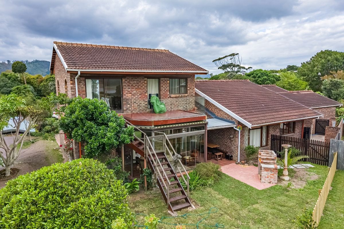 Rear view of a double-story brick house featuring a balcony, enclosed patio, external staircase, and a built-in brick braai area in the garden.