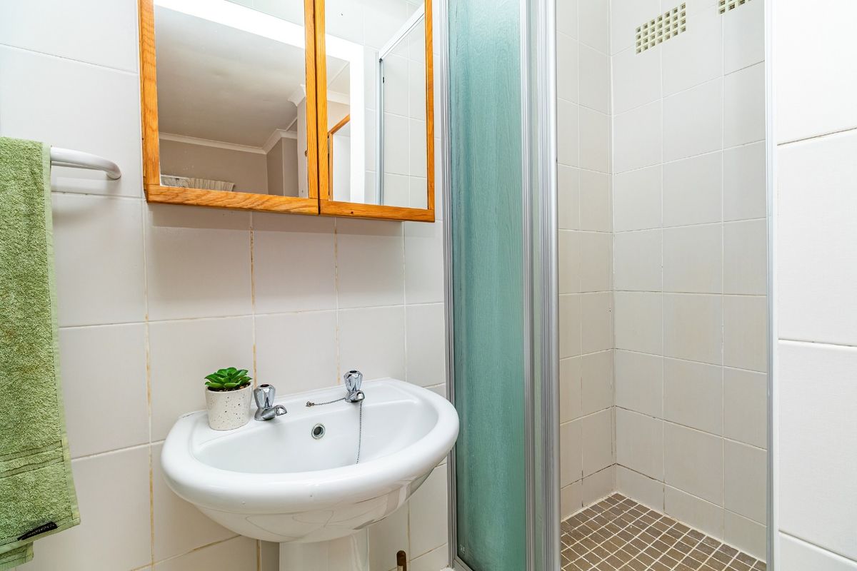 A functional bathroom featuring a pedestal basin, shower enclosure with tiled walls, and a wooden medicine cabinet.