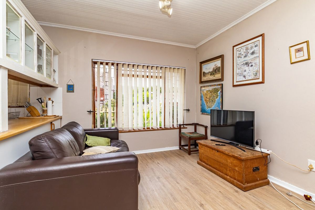 A living room featuring laminate flooring, a tongue and groove ceiling, and vertical blinds, with an adjacent kitchen counter area.