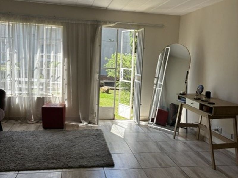 A bright living room featuring tiled flooring, a ceiling fan, and direct access to an outdoor garden area through a security gate.