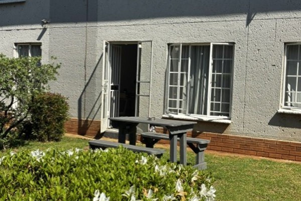Rear view of the apartment building featuring a textured concrete facade, multi-pane windows, and a small private garden area.