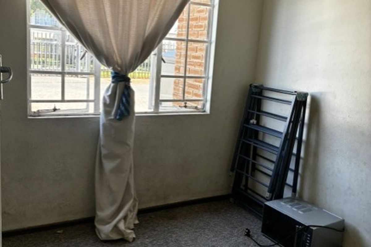 A vacant bedroom featuring carpet flooring and a window with curtain, requiring cosmetic updates to improve its overall condition.