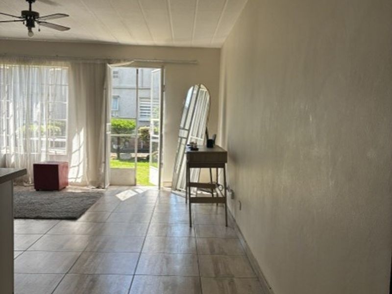 A bright, open-plan living area featuring neutral tiled flooring, a ceiling fan, and direct access to an outdoor patio through a glass sliding door.