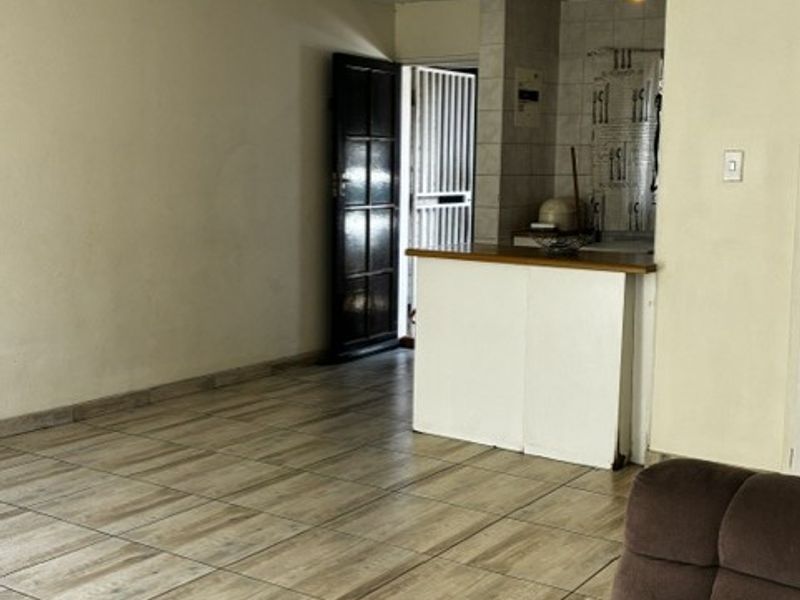 Open plan living area featuring tiled flooring, a ceiling fan, and a breakfast bar connecting to the kitchen space.