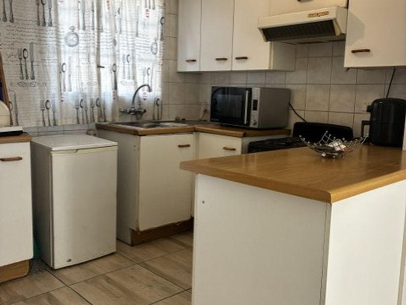 A functional kitchen featuring built-in cabinetry, a laminate countertop, tiled backsplash, and tiled flooring, offering potential for modernization and aesthetic updates.