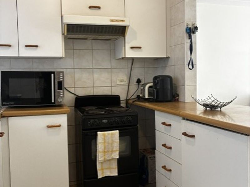 A compact kitchen featuring white cabinetry, laminate countertops, tiled backsplash, and tiled flooring, offering a functional layout with potential for modern updates.
