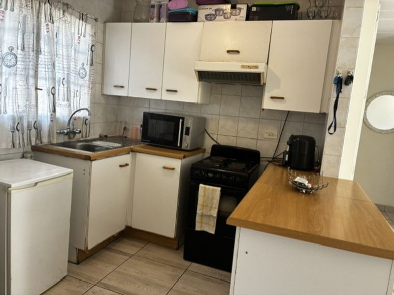 Compact kitchen featuring white cabinetry, laminate countertops, tiled backsplash, and integrated extractor fan, offering a functional layout with potential for modern updates.
