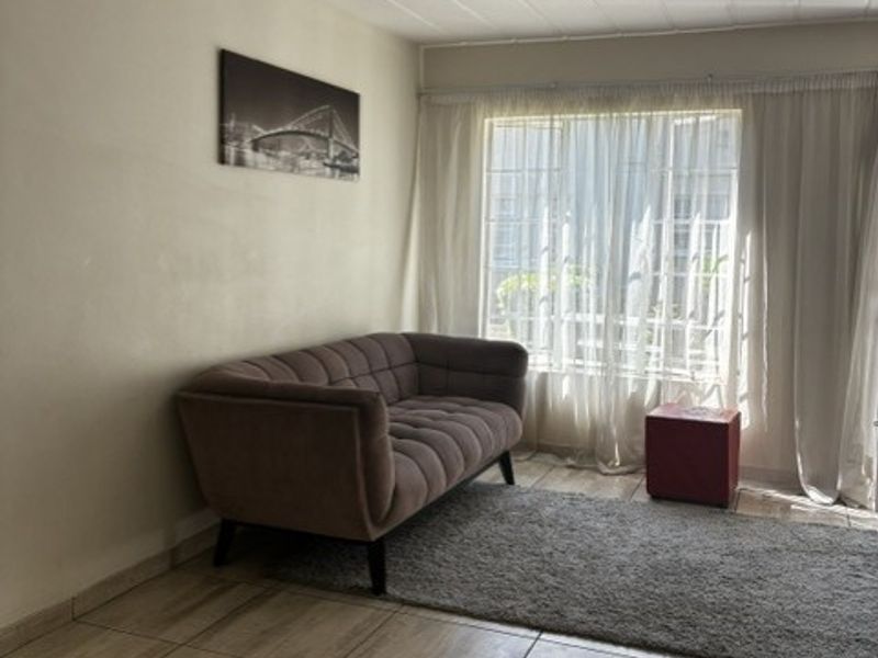 A living room featuring tiled flooring, a ceiling fan, and a large window allowing natural light.