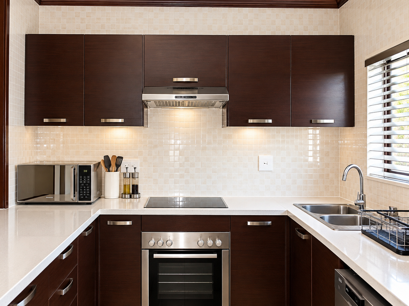 A well-maintained kitchen featuring dark wood cabinetry, quartz countertops, stainless steel appliances, and a tiled backsplash with natural light from the window.