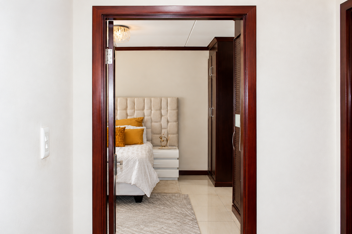 A view through a wooden doorway into a bedroom featuring a built-in wardrobe and tiled flooring.