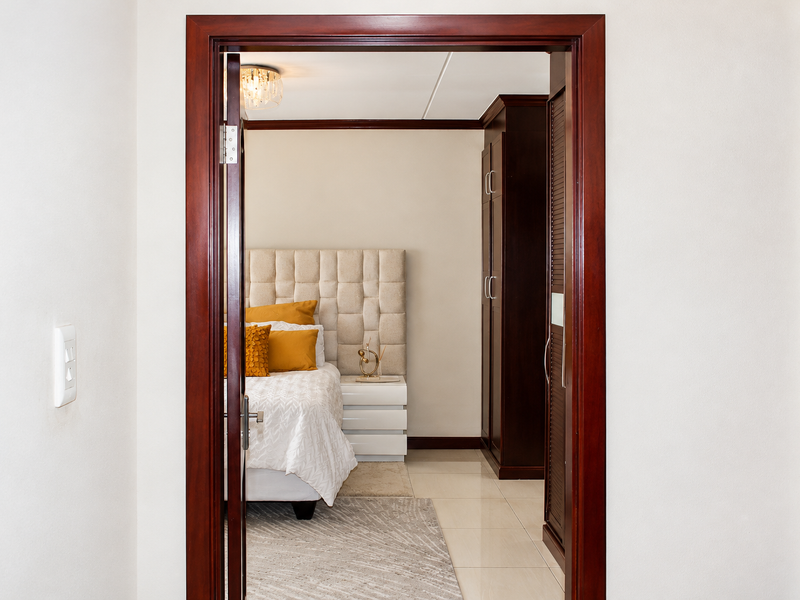 A view through a wooden doorway into a bedroom featuring a built-in wardrobe and tiled flooring.