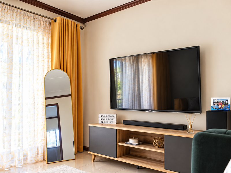 A well-maintained living room featuring crown molding, tiled flooring, and a wall-mounted television setup with neutral wall tones.