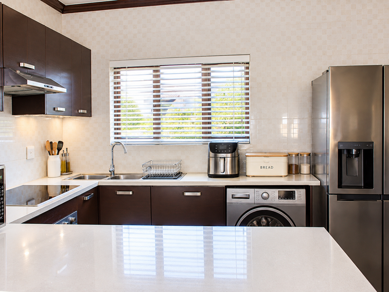 A well-maintained kitchen featuring dark wood cabinetry, stone countertops, integrated appliances, and a tiled backsplash with natural light from the window.