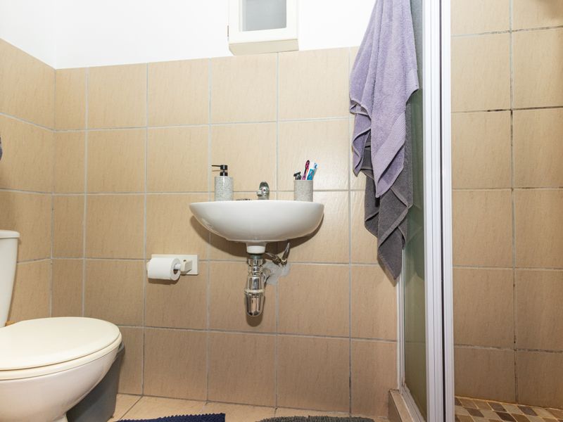 Compact bathroom featuring a wall-mounted basin, toilet, and shower enclosure with neutral ceramic wall tiling.