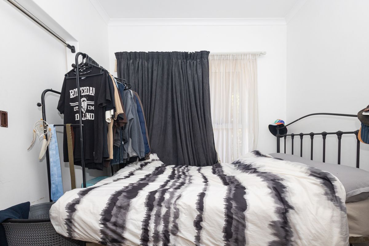 A bedroom featuring white walls, coving, and a window dressed with layered curtains.