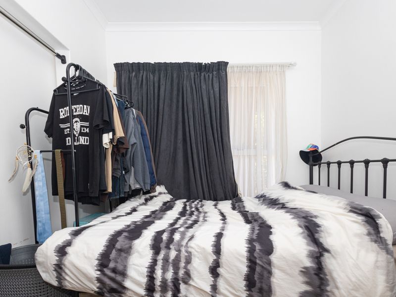 A bedroom featuring white walls, coving, and a window dressed with layered curtains.