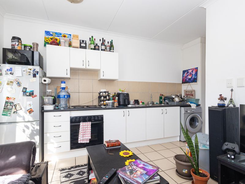 Open plan kitchen area featuring white cabinetry, tiled backsplash, built-in oven, and integrated laundry plumbing, providing a functional layout for compact living.