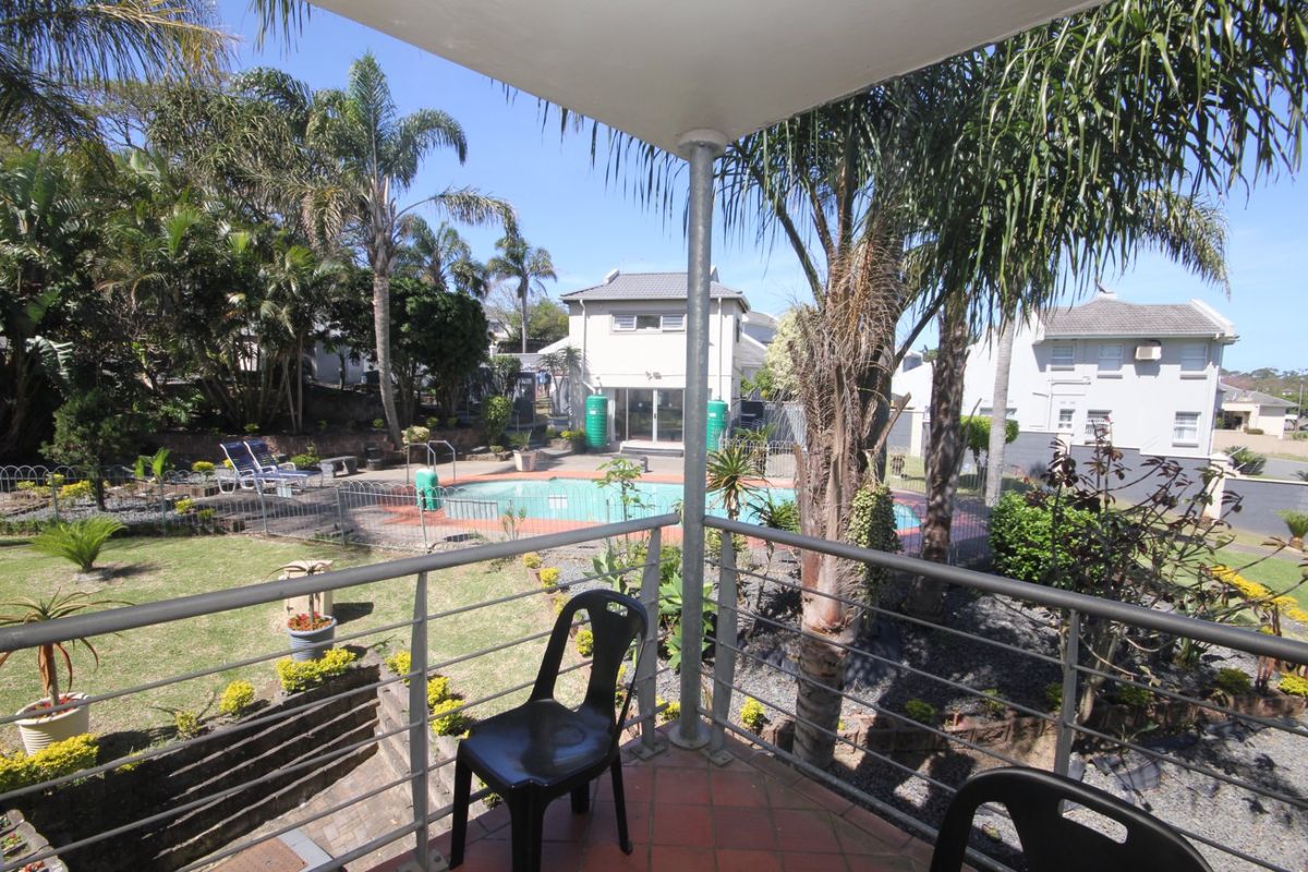 Elevated balcony overlooking a private garden and swimming pool area, featuring a metal balustrade and tiled flooring.