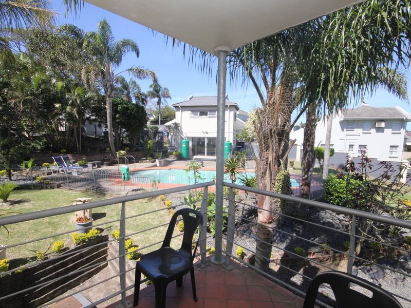Elevated balcony overlooking a private garden and swimming pool area, featuring a metal balustrade and tiled flooring.