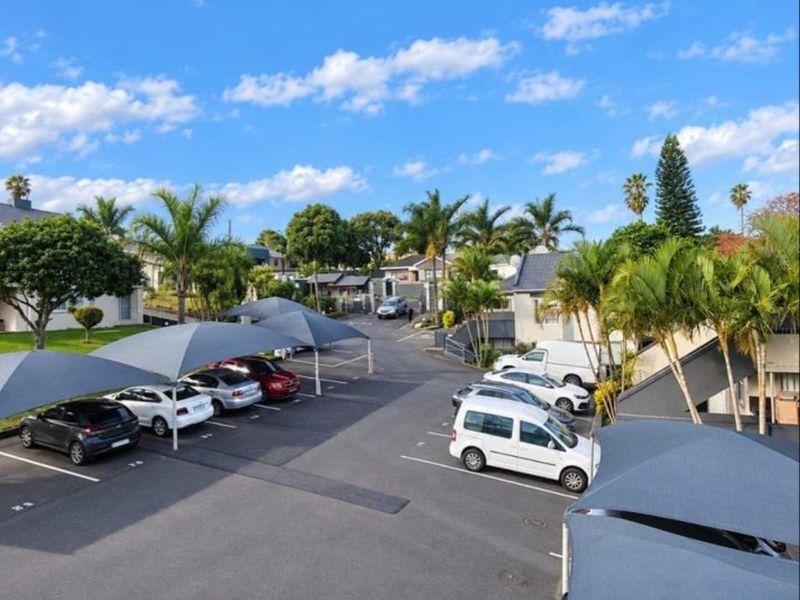 An elevated view of the townhouse complex parking area featuring multiple shade cloth carports and paved parking bays within a landscaped estate setting.