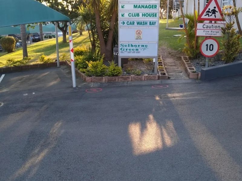 Entrance area of Selborne Green residential complex featuring directional signage, paved driveway, and shaded parking facilities.