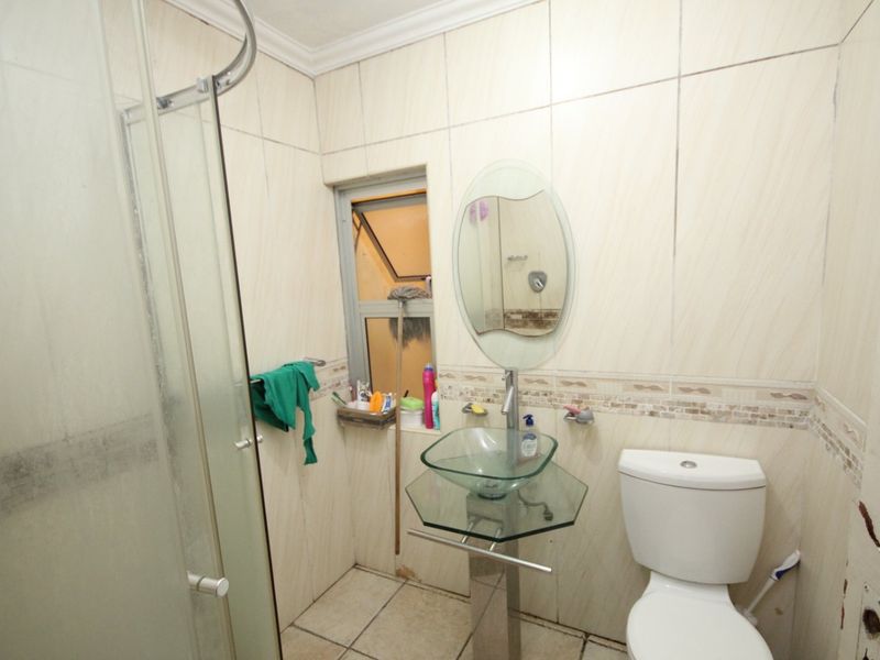 Compact bathroom featuring a glass shower enclosure, pedestal basin, and tiled finishes. The space requires maintenance and cosmetic updates to improve its condition.