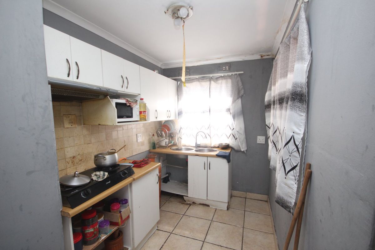 A compact kitchen featuring built-in cabinetry, a double sink, and tiled flooring, currently requiring maintenance and cosmetic updates to improve its overall condition.