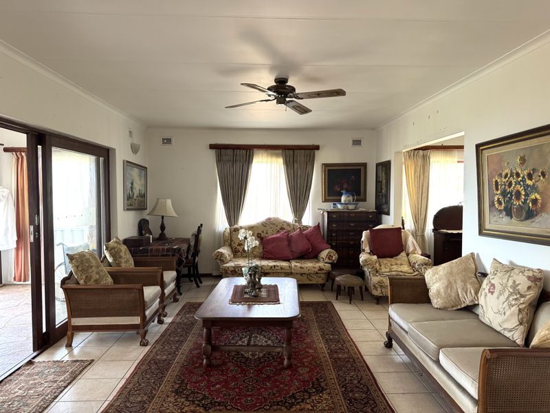 A spacious living room featuring tiled flooring, a ceiling fan, and large sliding glass doors that provide access to the outdoor area.
