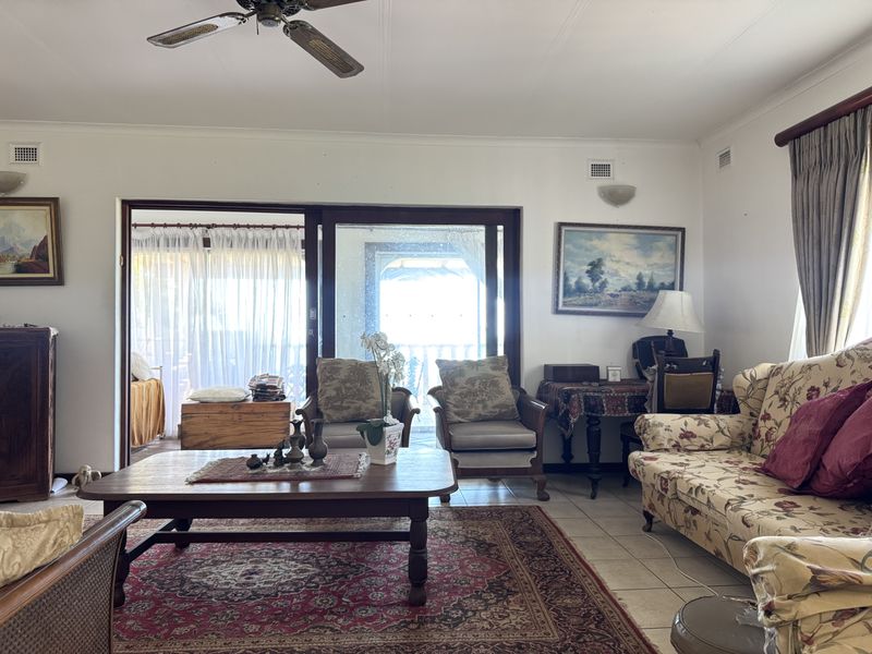 A spacious living room featuring tiled flooring, a ceiling fan, and large sliding glass doors that provide access to an adjoining patio area.